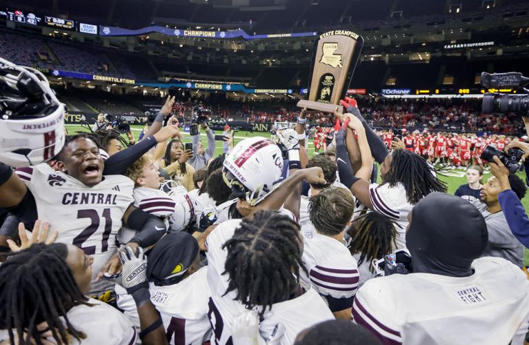 A high school football team crowded together on the field lifting the state championship trophy inside the Caesars Superdome.